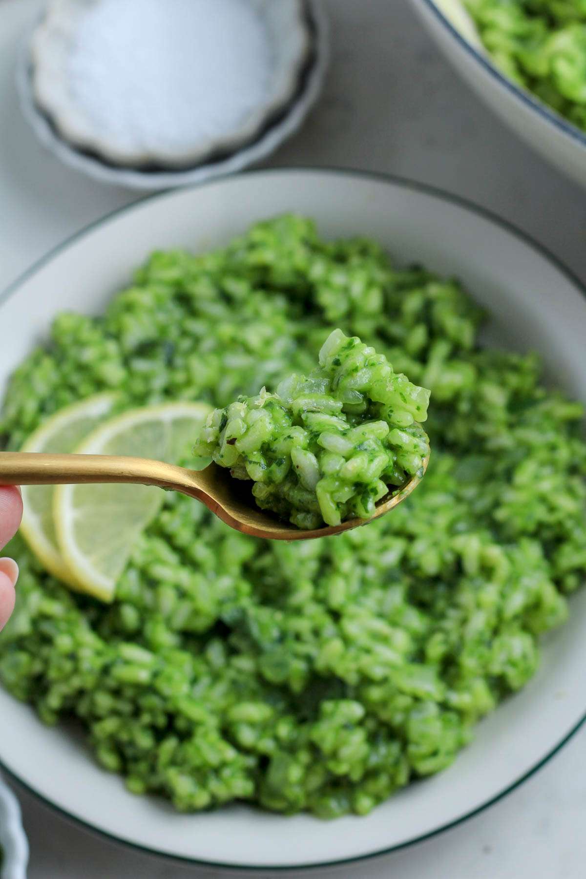 A gold spoon holding a scoop of vegan pesto risotto over a plate of vegan risotto.