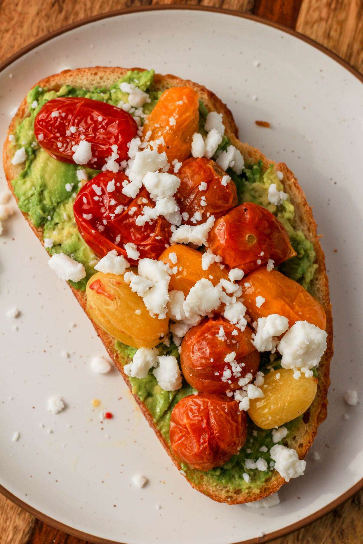 Dairy-free avocado toast topped with roasted grape tomatoes and vegan feta on a white plate.