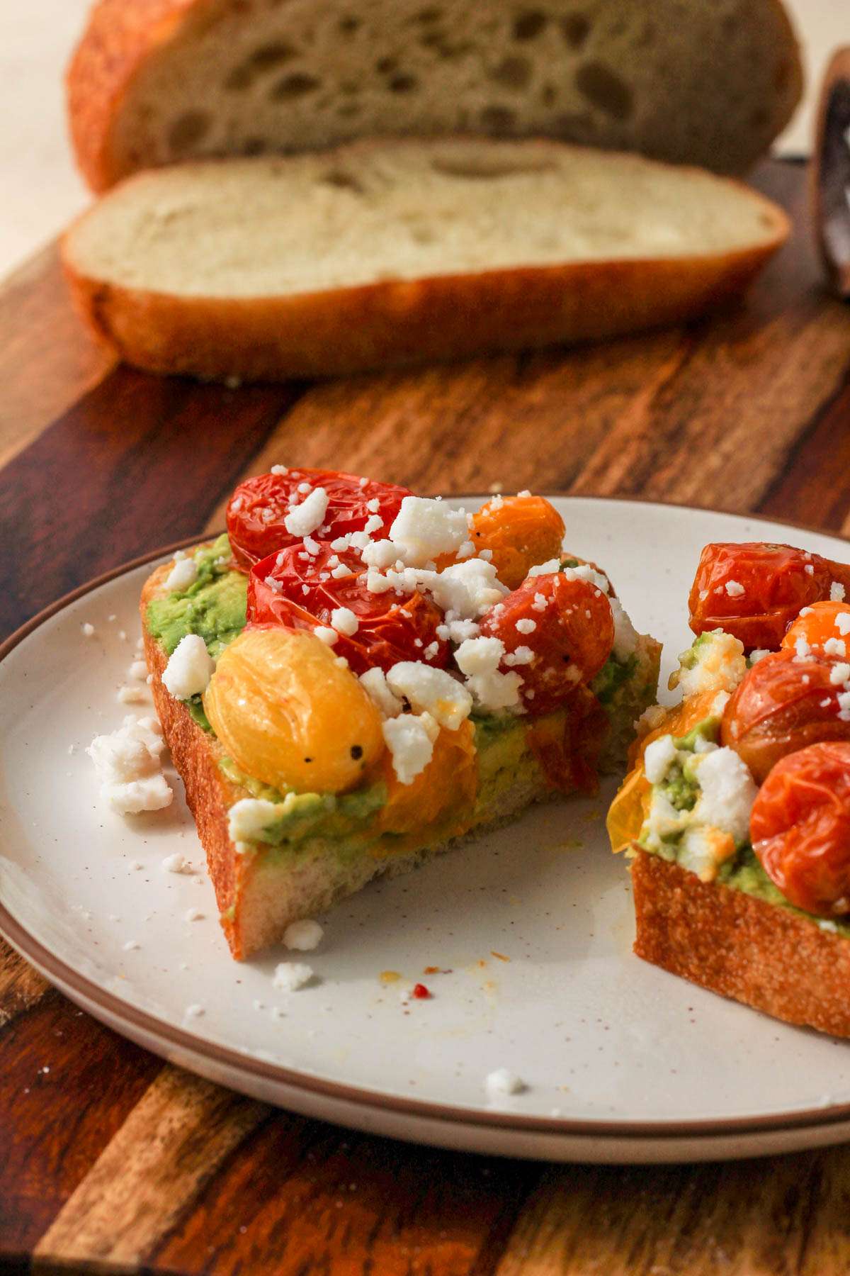 A small white plate with a brown rim topped with vegan avocado toast with roasted tomatoes and feta.