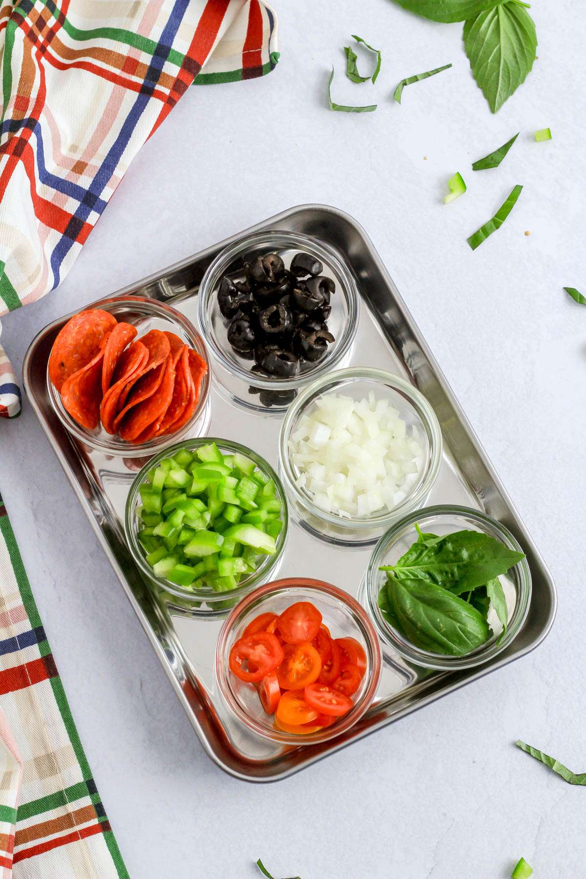 Six different toppings for pizza toast in small bowls in a small sheet pan.