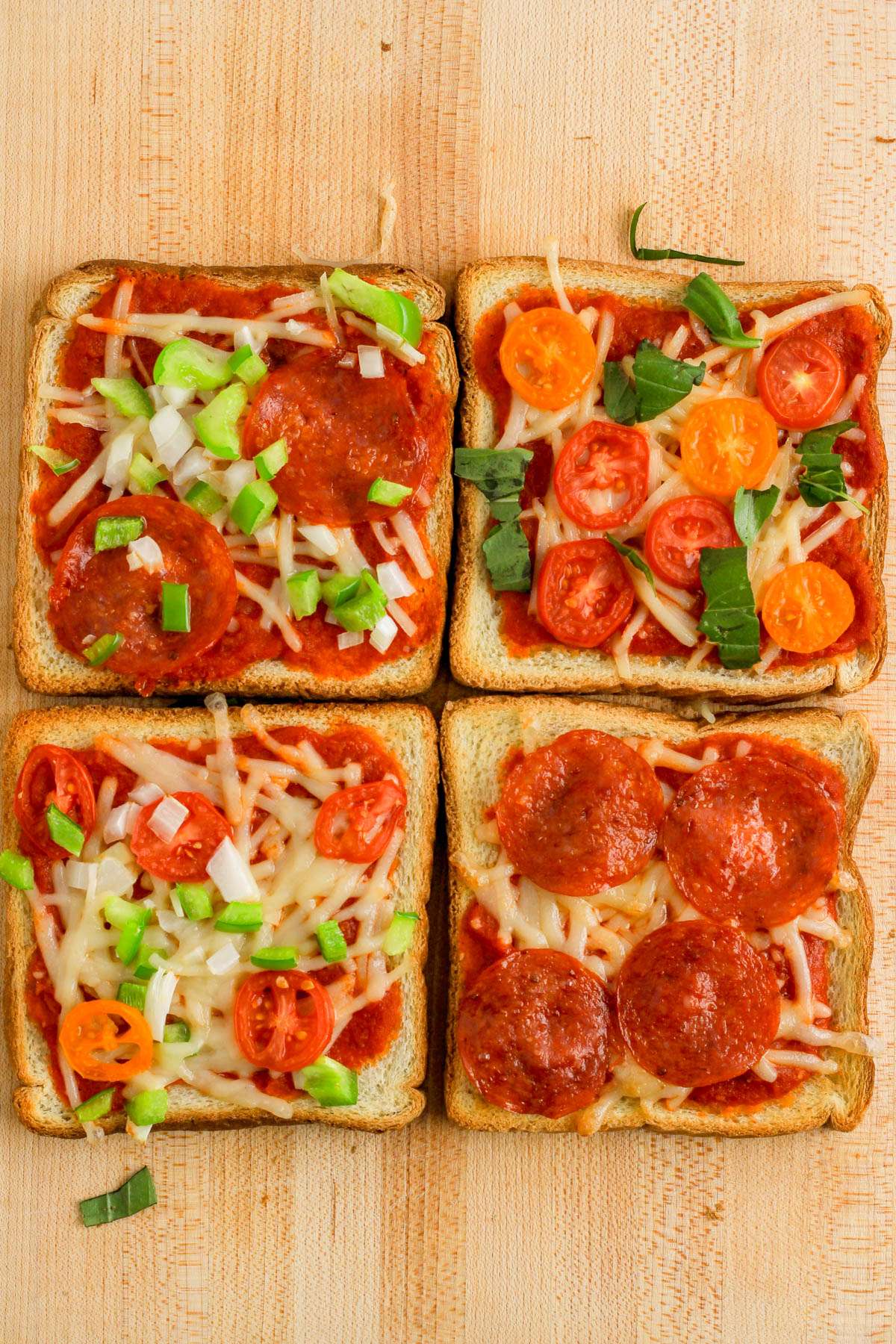A wooden cutting board with four slices of pizza toast topped in different ways.