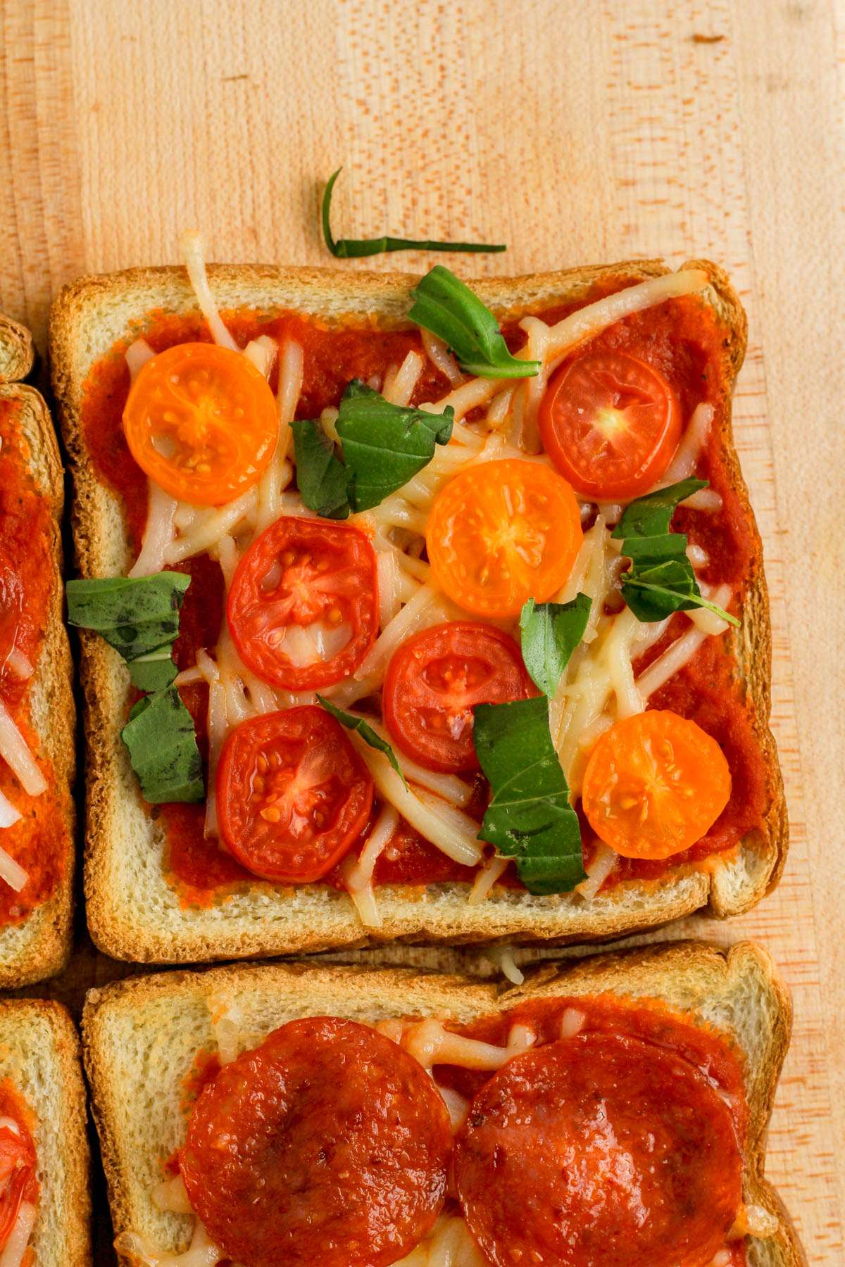 A dairy-free pizza toast with tomatoes and basil on a wooden cutting board.
