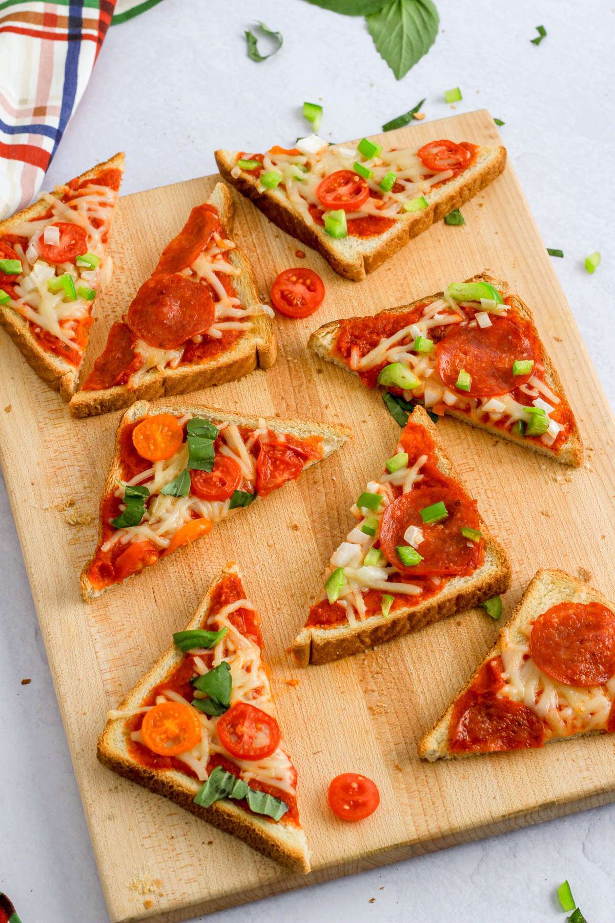 A wooden cutting board on a white counter with various flavors of dairy-free pizza toast on the board.