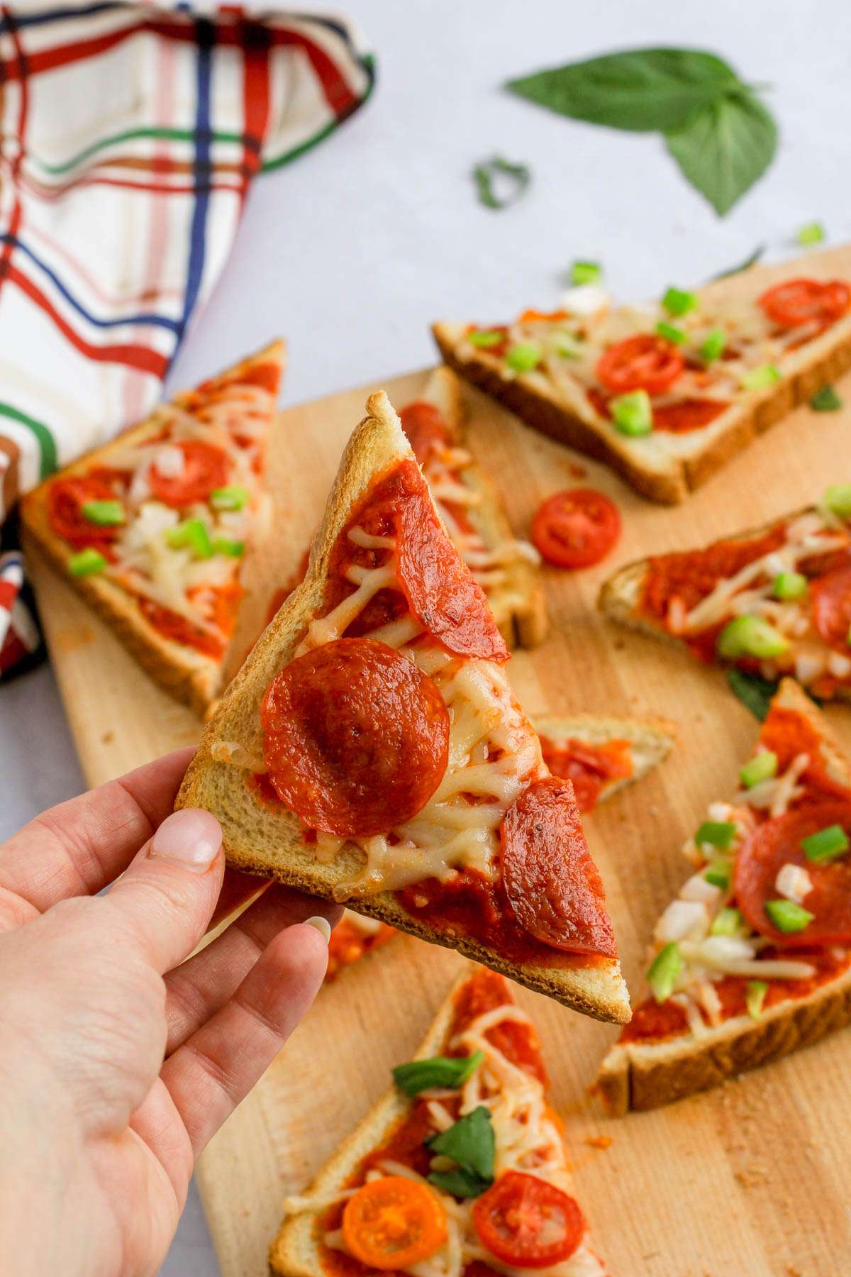 A hand holding a triangular slice of dairy-free pizza toast.