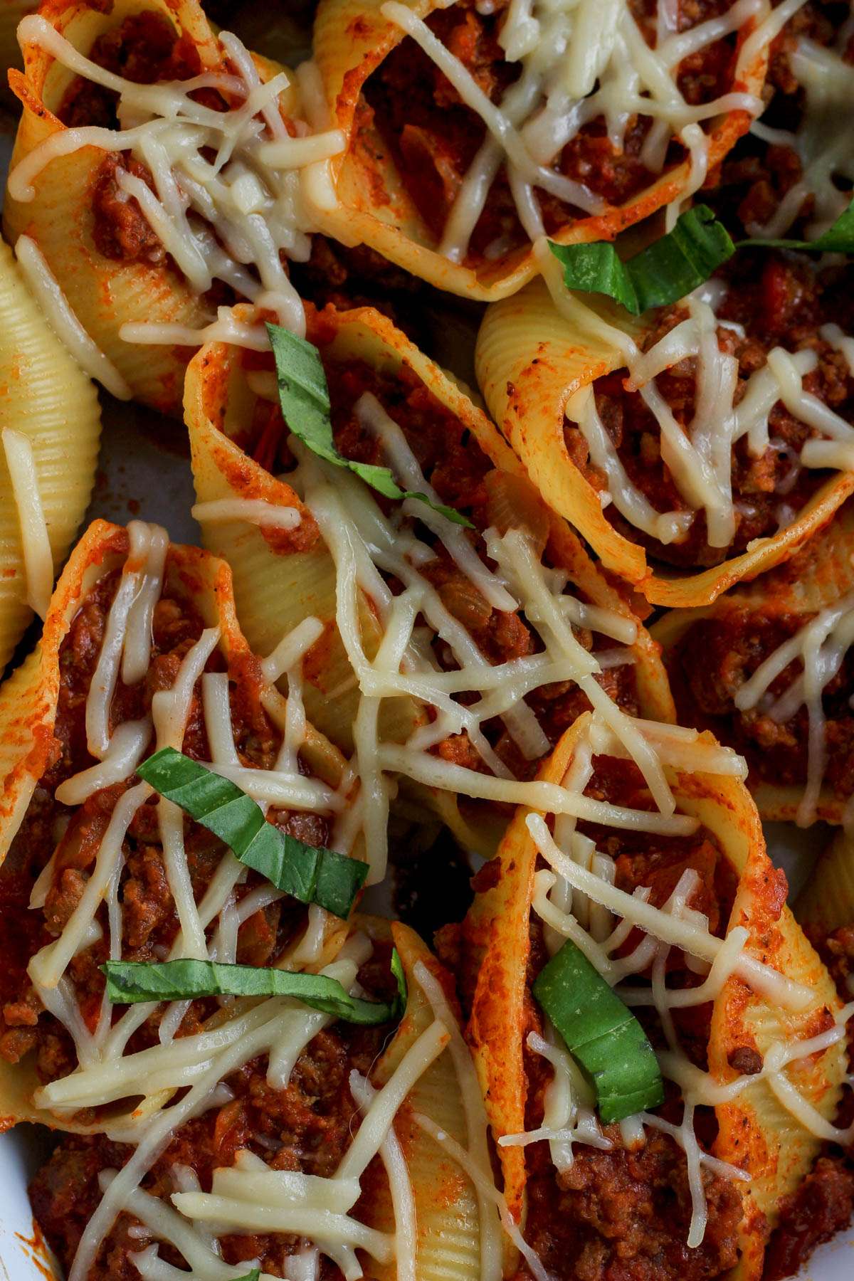 A close up of baked stuffed shells with meat sauce topped with vegan cheese and basil.