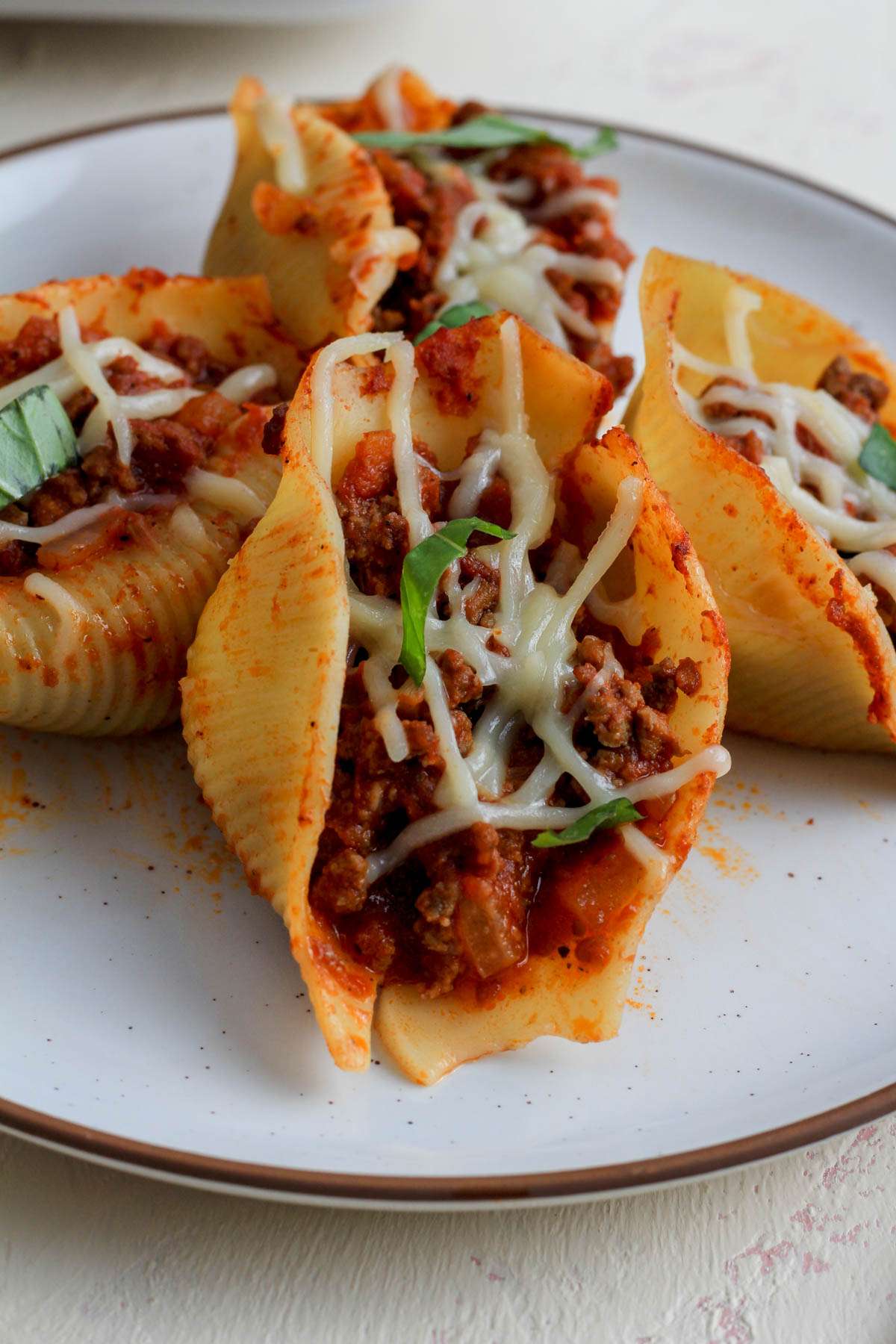 A white plate with jumbo stuffed shells with meat sauce topped with vegan cheese and basil.