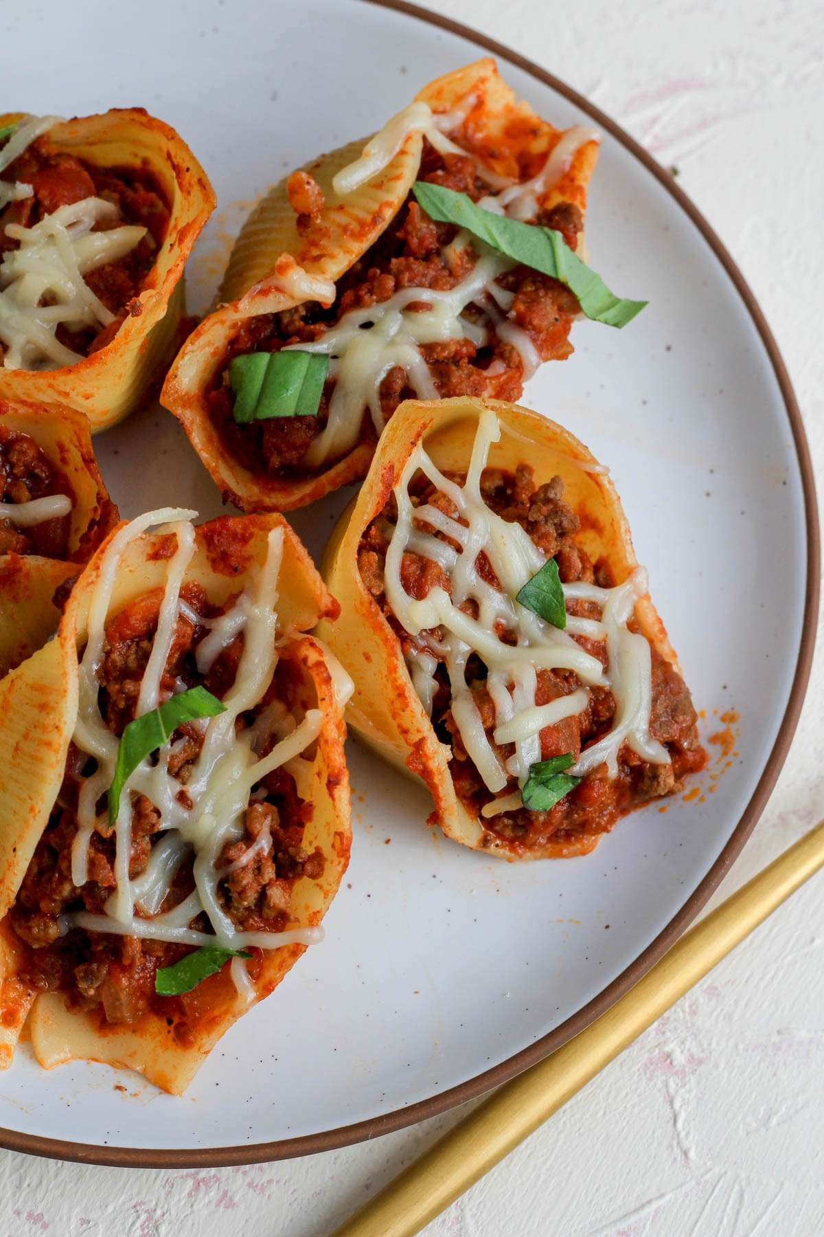 A top down picture of dairy-free stuffed shells with meat sauce on a white plate with a brown rim.