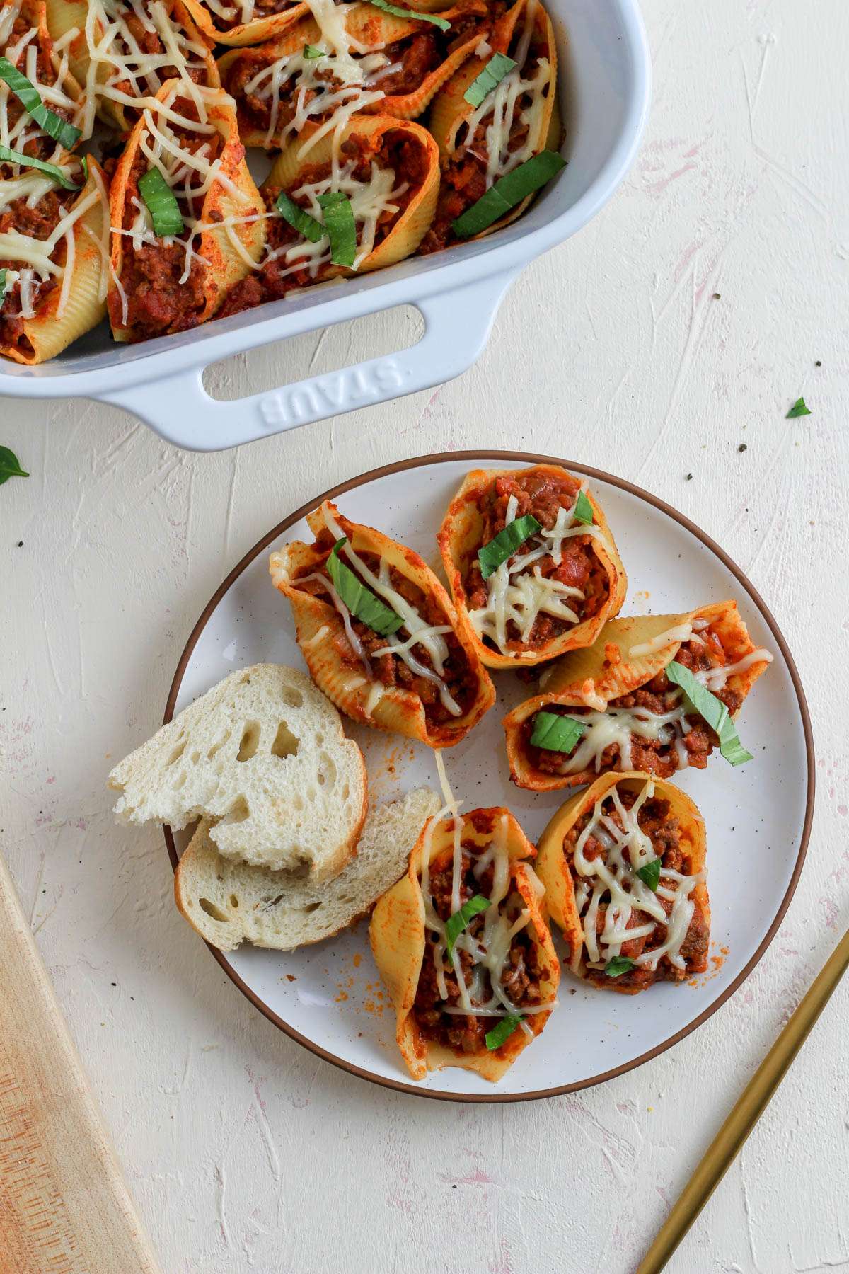 Jumbo stuffed shells with meat sauce on a white plate with a side of bread and a baking dish filled with jumbo shells in the back left.