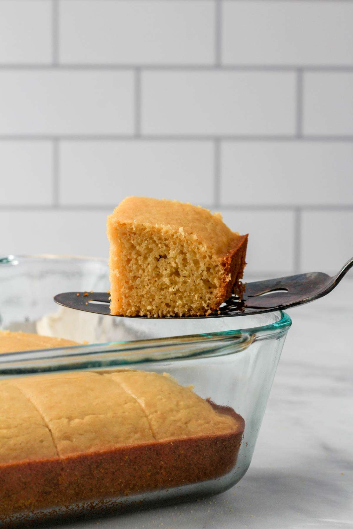 A glass dish with a cake serve holding a slice of gluten-free dairy-free cornbread over the baking dish.