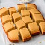 A close up of sixteen small slices of gluten-free dairy-free cornbread on a piece of parchment paper.