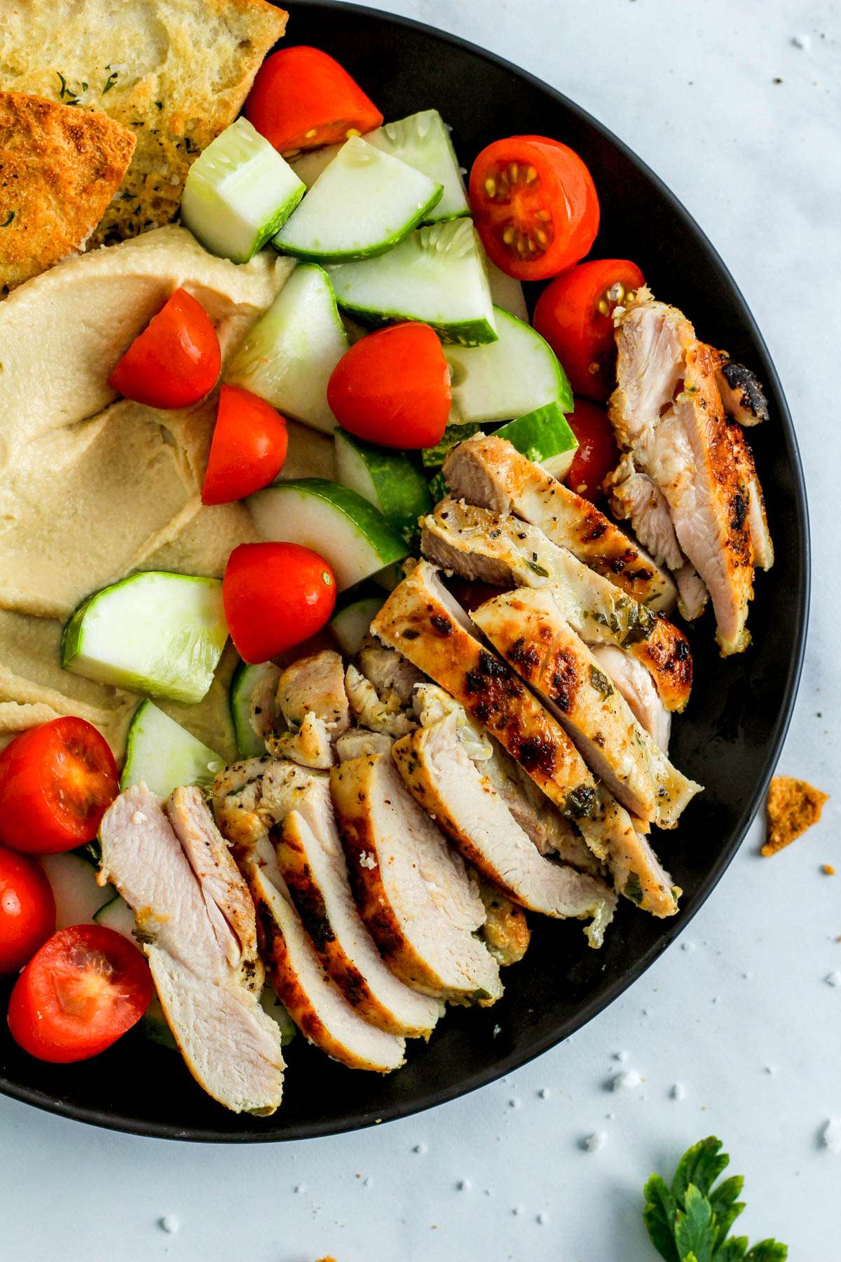 A black plate on a white counter with a greek chicken hummus bowl.