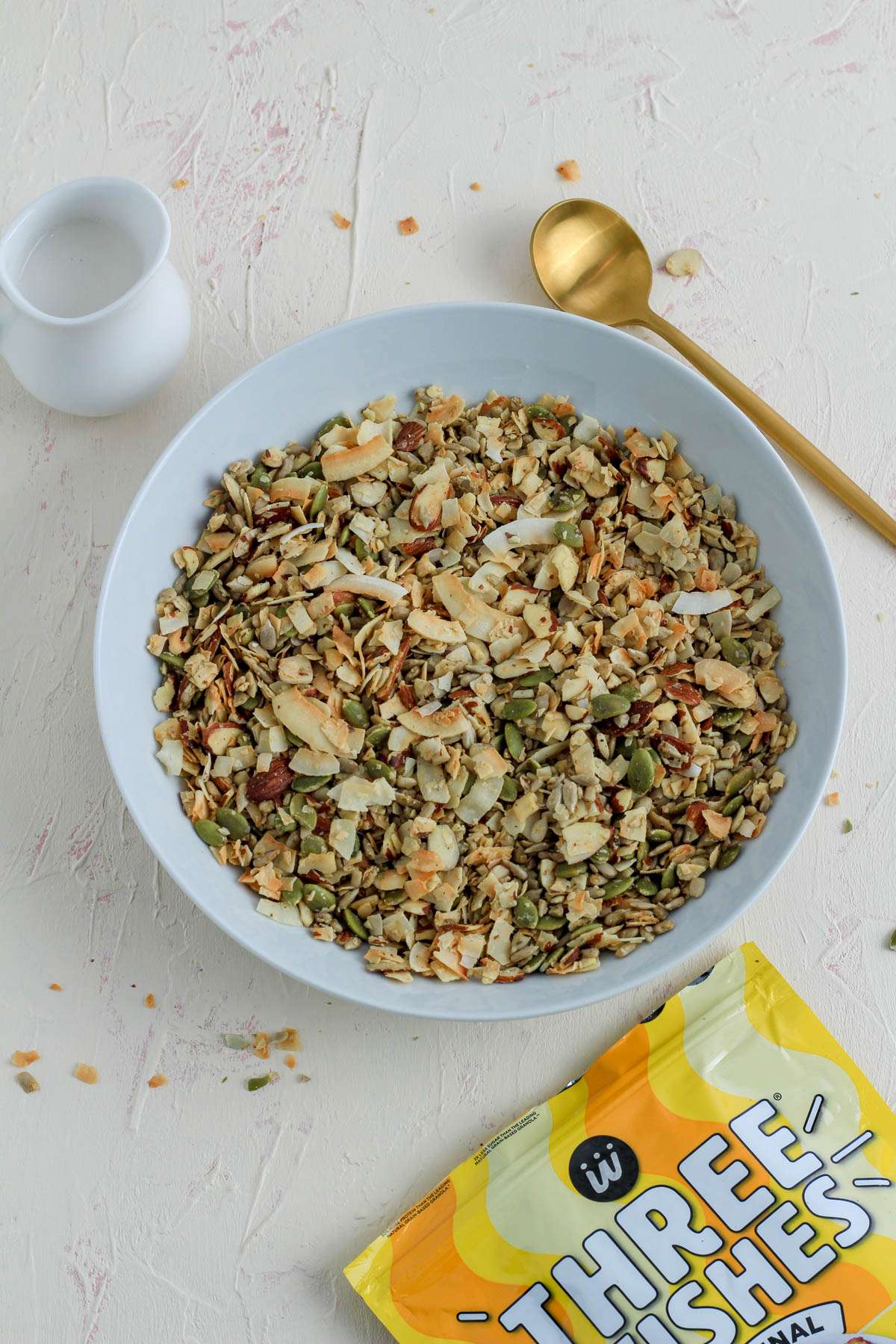 A white bowl with Three Wishes Original Grain Free Granola with a gold spoon above the bowl and a package of the granola in the bottom right.