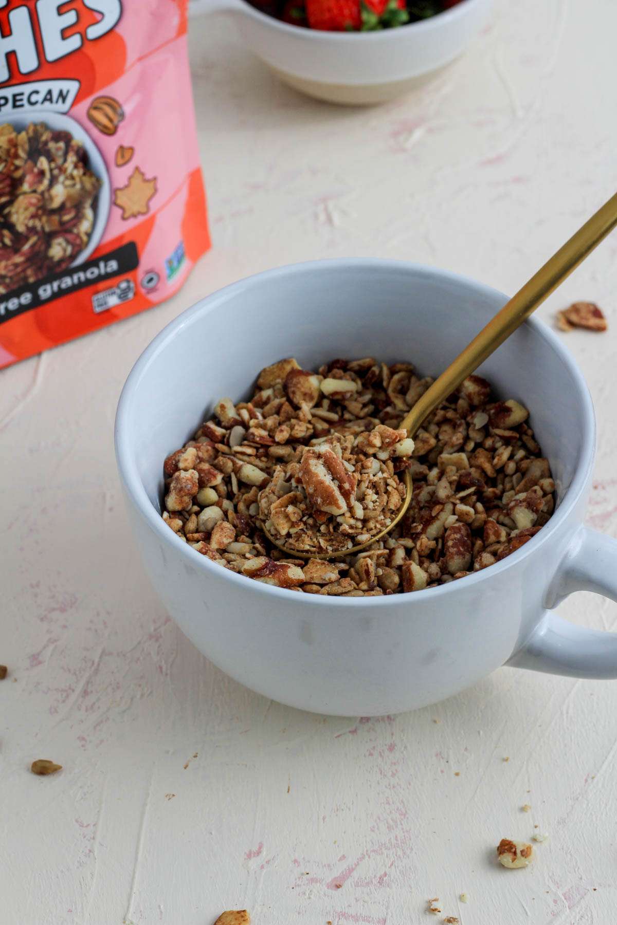 A large white mug filled with maple pecan grain free granola with a gold spoon in the top right.