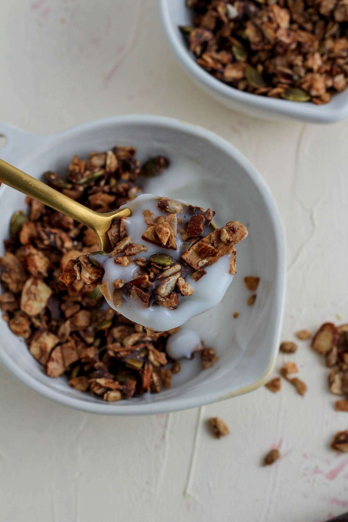 A small white bowl with vegan yogurt topped with Chocolate Almond grain free granola with a spoon holding a scoop of the yogurt and granola over the bowl.
