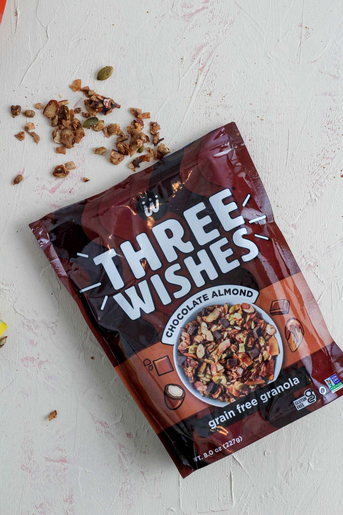 A cream counter with a package of Chocolate Almond grain free granola opened with a sprinkle of granola coming out of the top.