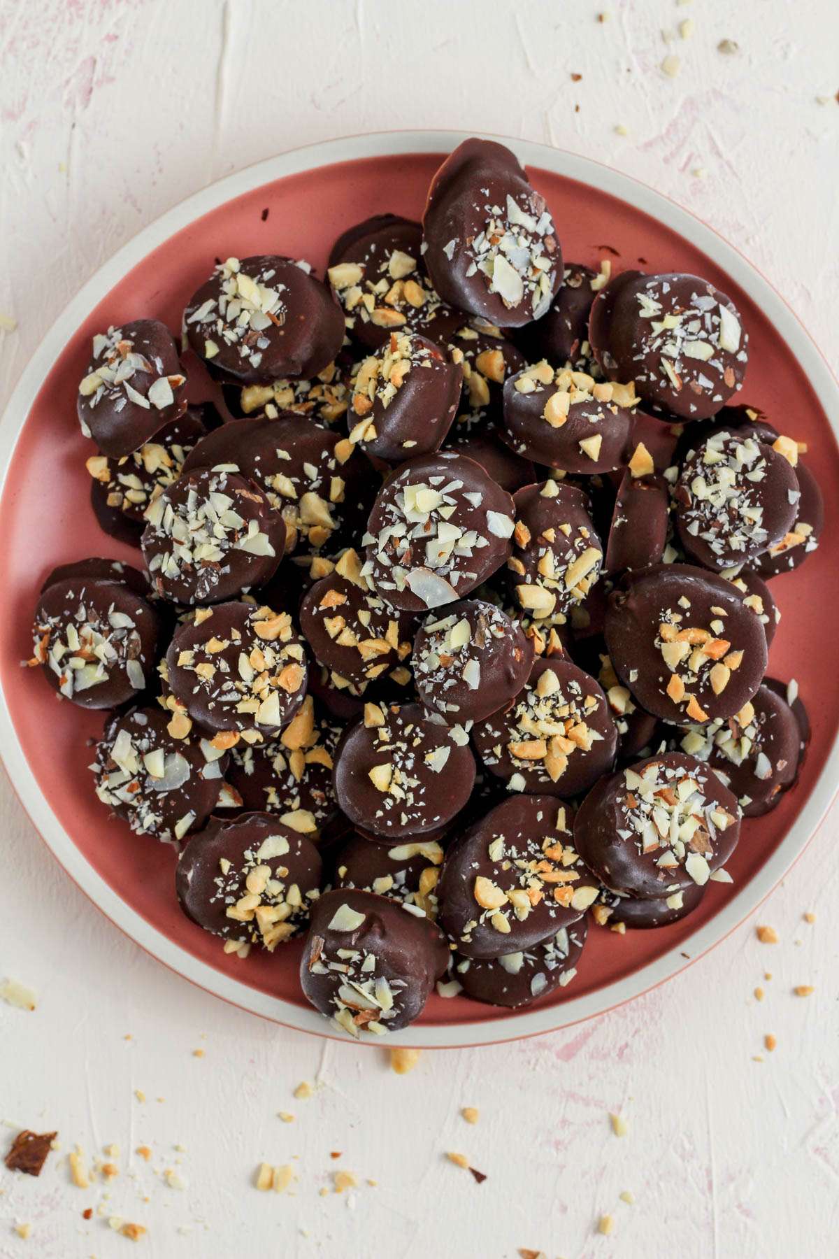 A stack of dairy-free chocolate dipped banana bites topped with crushed peanuts and sliced almonds on a pink plate.