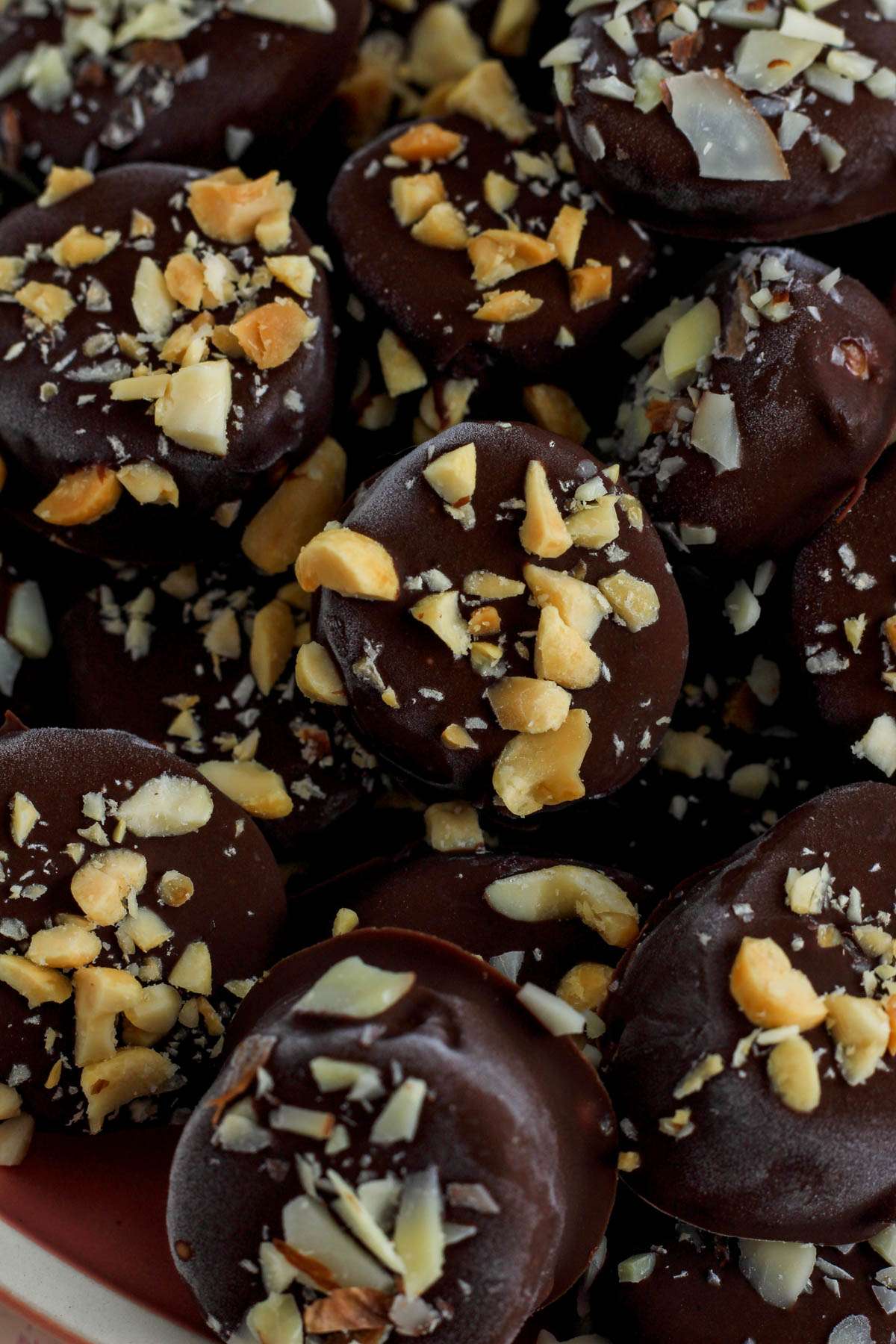 A pile of chocolate dipped banana bites with salted peanuts and sliced almonds.