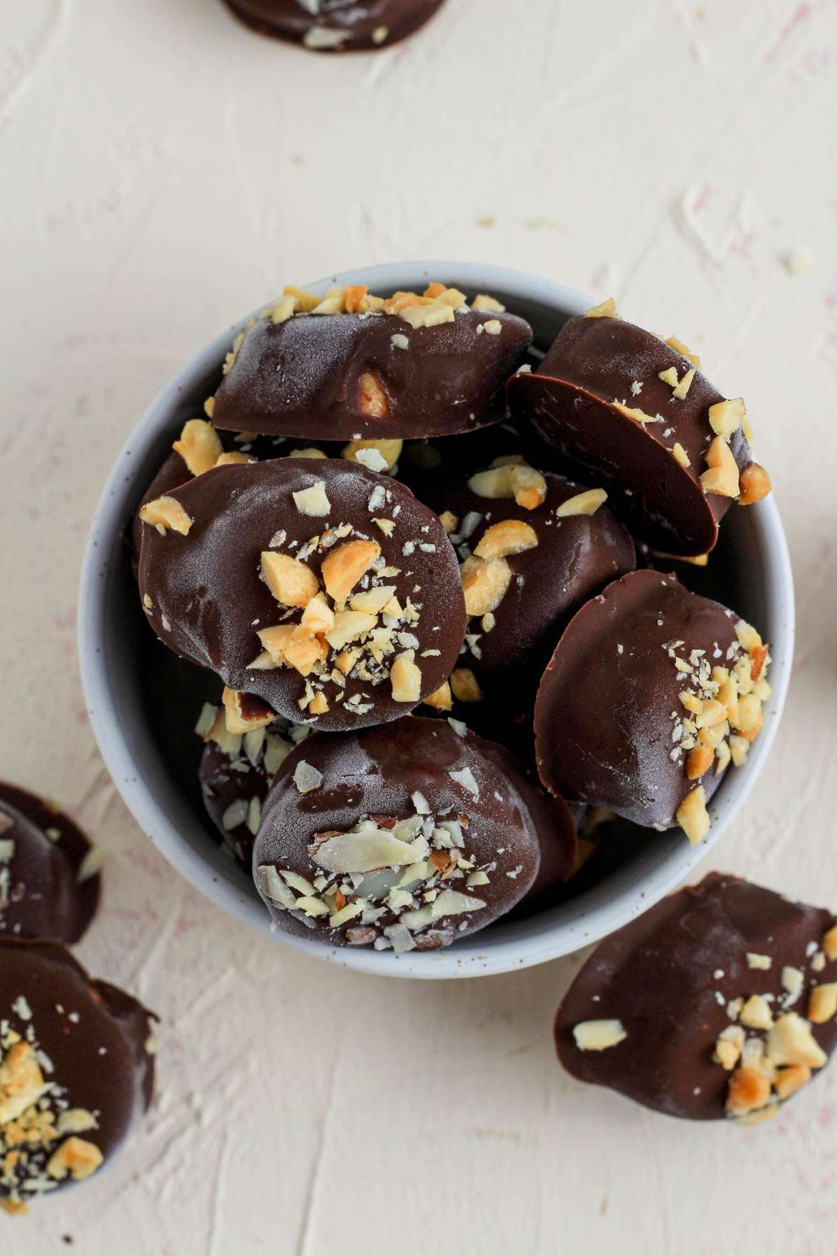 A small white bowl with frozen chocolate dipped banana bites on a white counter.