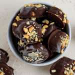 Vegan chocolate dipped banana bites in a small white bowl with peanuts and almonds.
