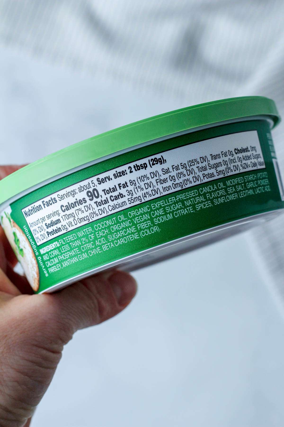 A hand holding a tub of dairy-free Boursin cheese showing the nutritional information.
