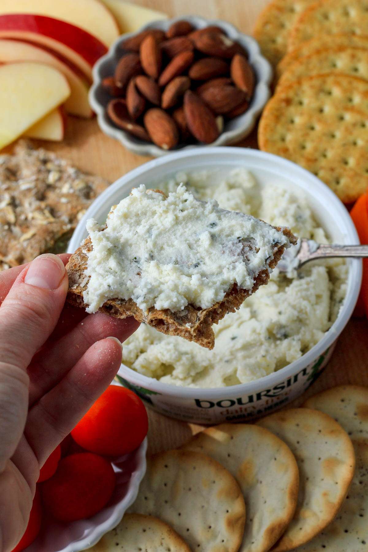 A hand holding a cracker topped with Boursin dairy-free cheese spread.