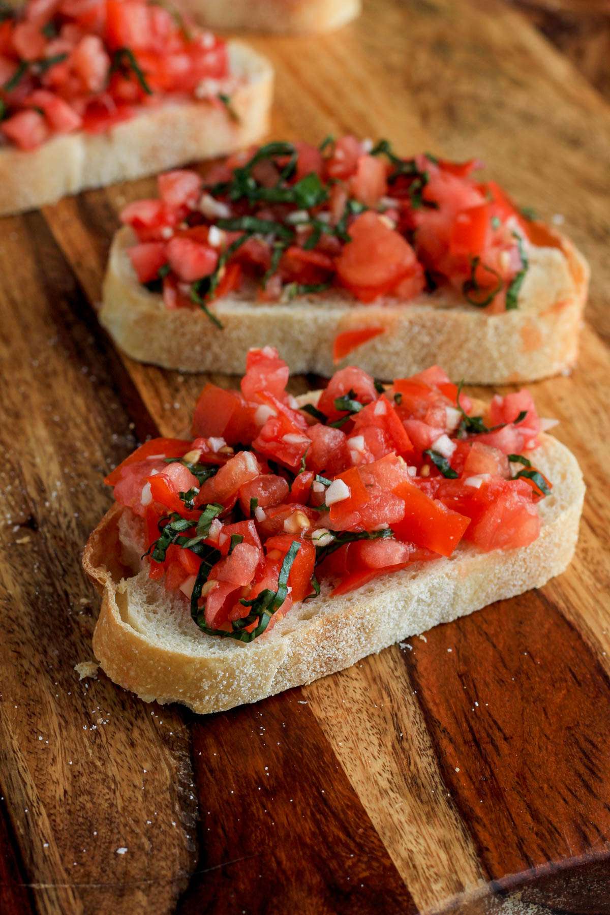 A piece of bruschetta toast on a wooden cutting board.
