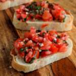 A close up of two pieces of bruschetta on toast on a wooden counter.