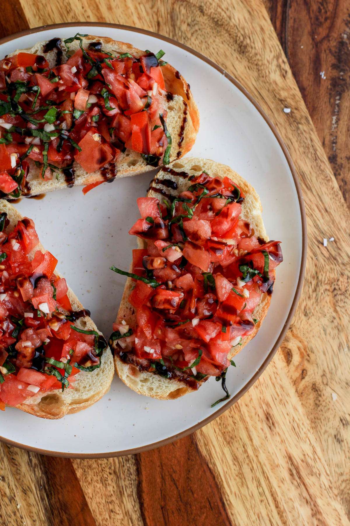 A white plate on a wooden counter with pieces of bruschetta drizzled with balsamic glaze.