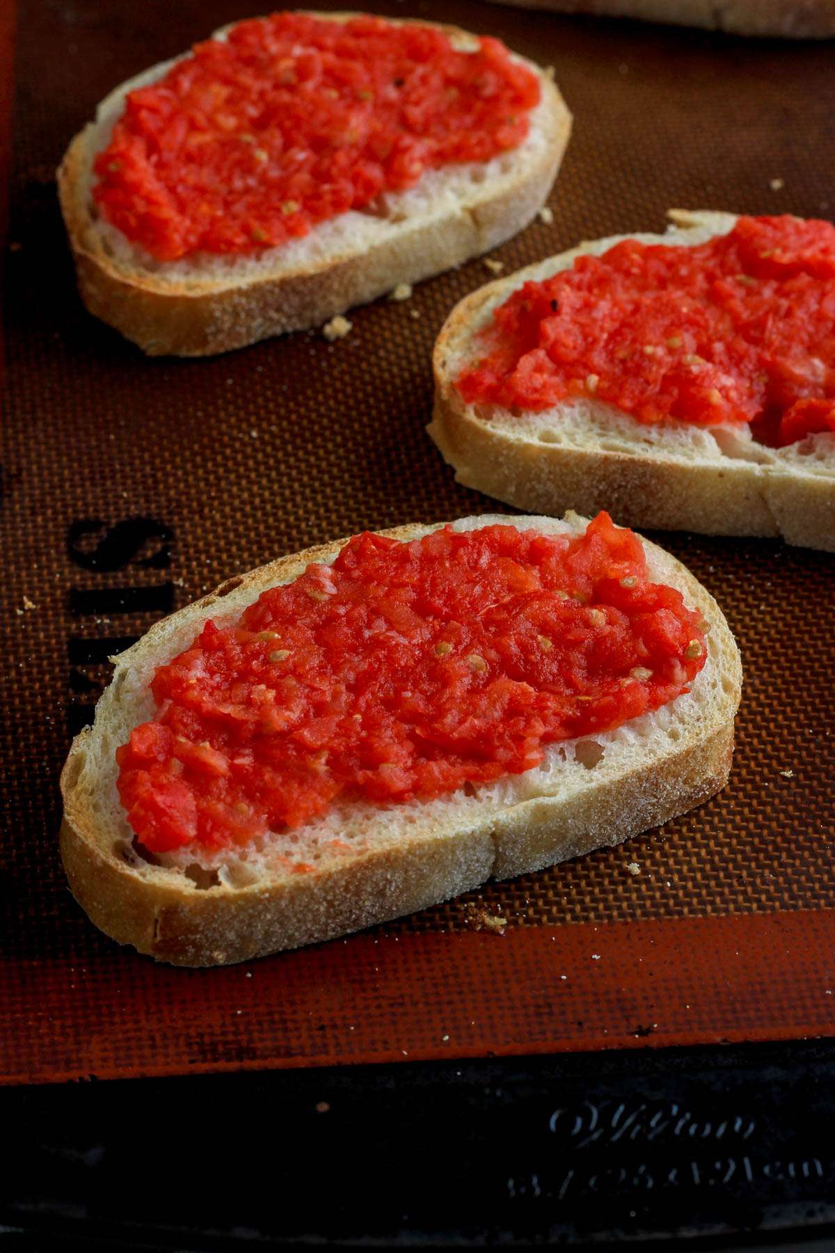 A close up of pan con tomate on a lined baking sheet.