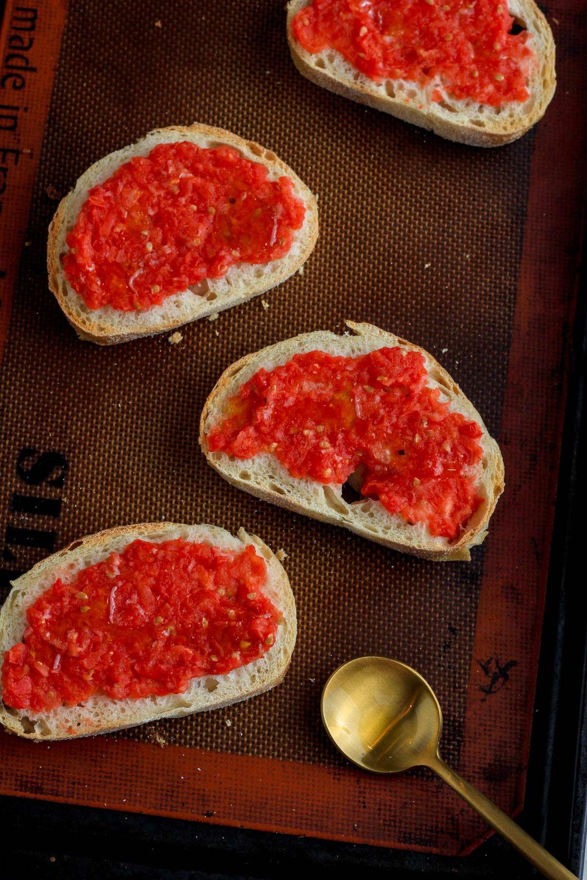 A top down picture of four slices of pan con tomate on a baking sheet after being drizzled with olive oil.