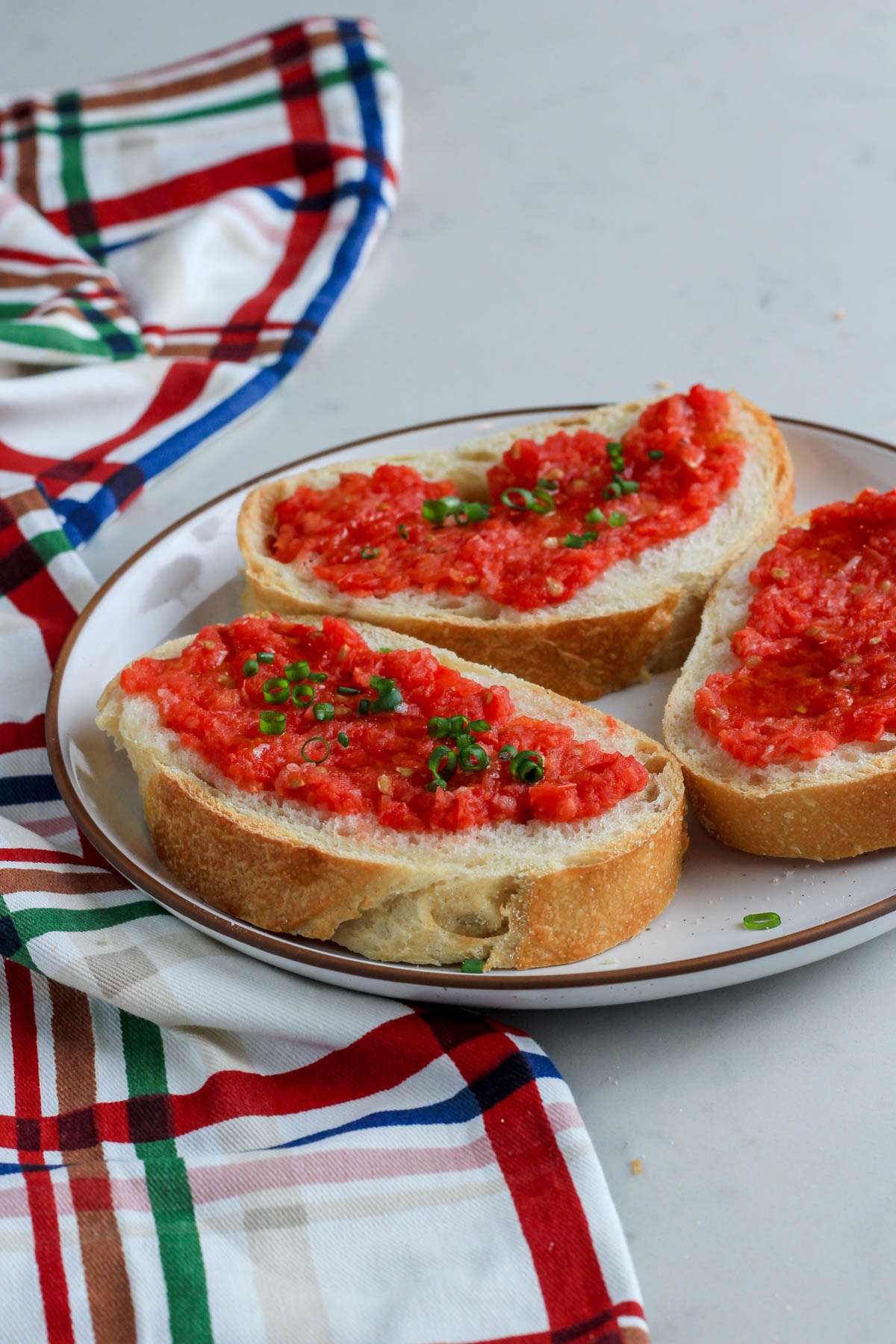Three pieces of vegan pan con tomate on a white plate with a brown rim on a white counter.