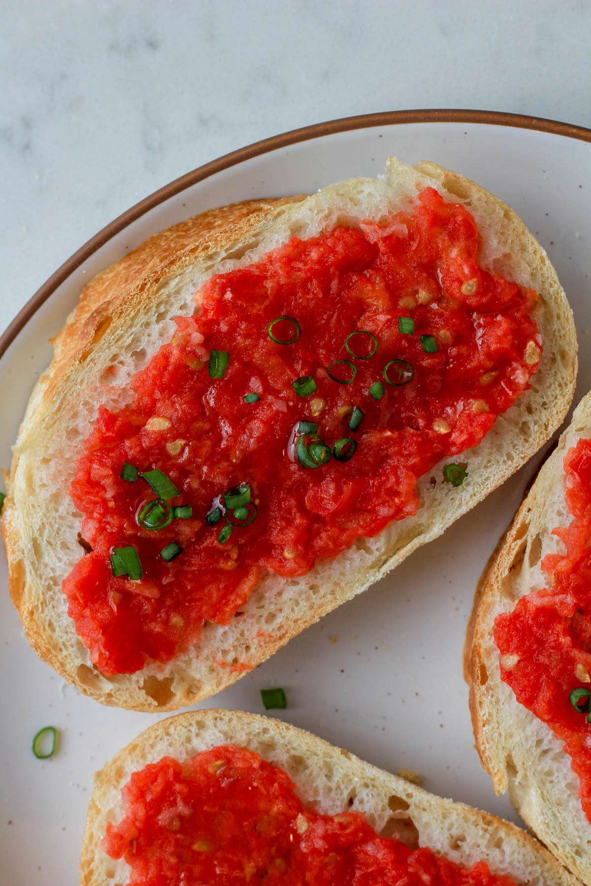 A close up of a vegan pan con tomate on a white plate with a brown rim.