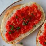 Pan con tomate topped with green onion and olive oil on a white plate with a brown rim.