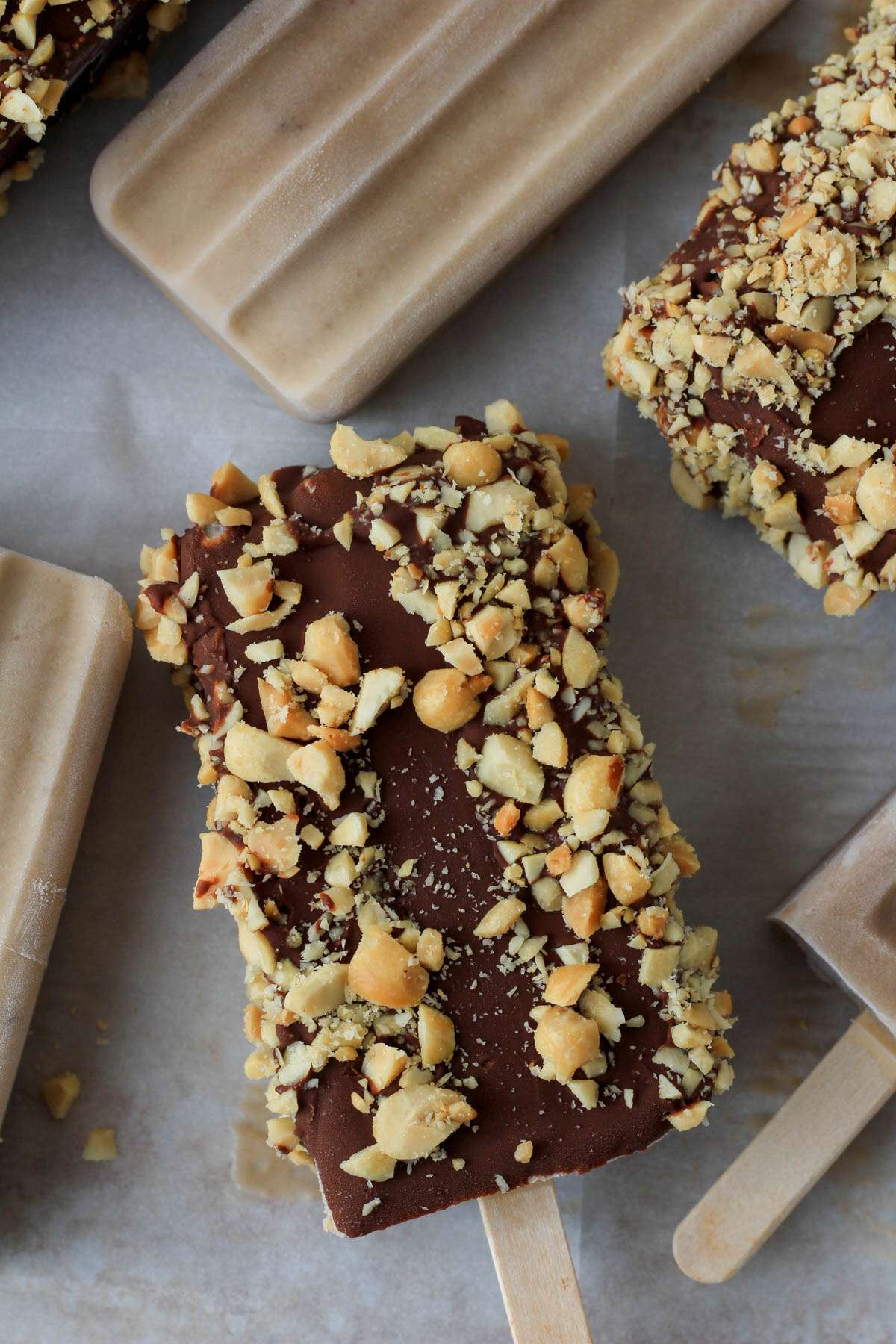 A parchment paper lined baking sheet with plain and chocolate dipped peanut butter banana popsicles.
