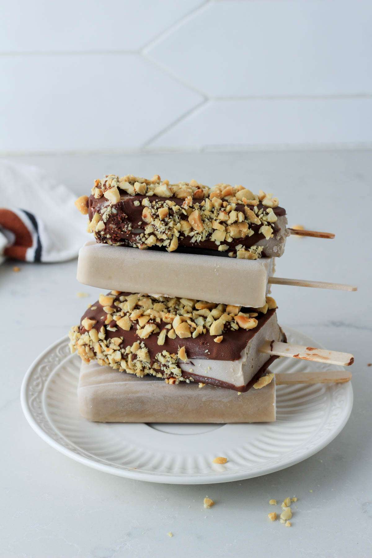A small white plate on a white counter with four peanut butter banana popsicles stacked on top.