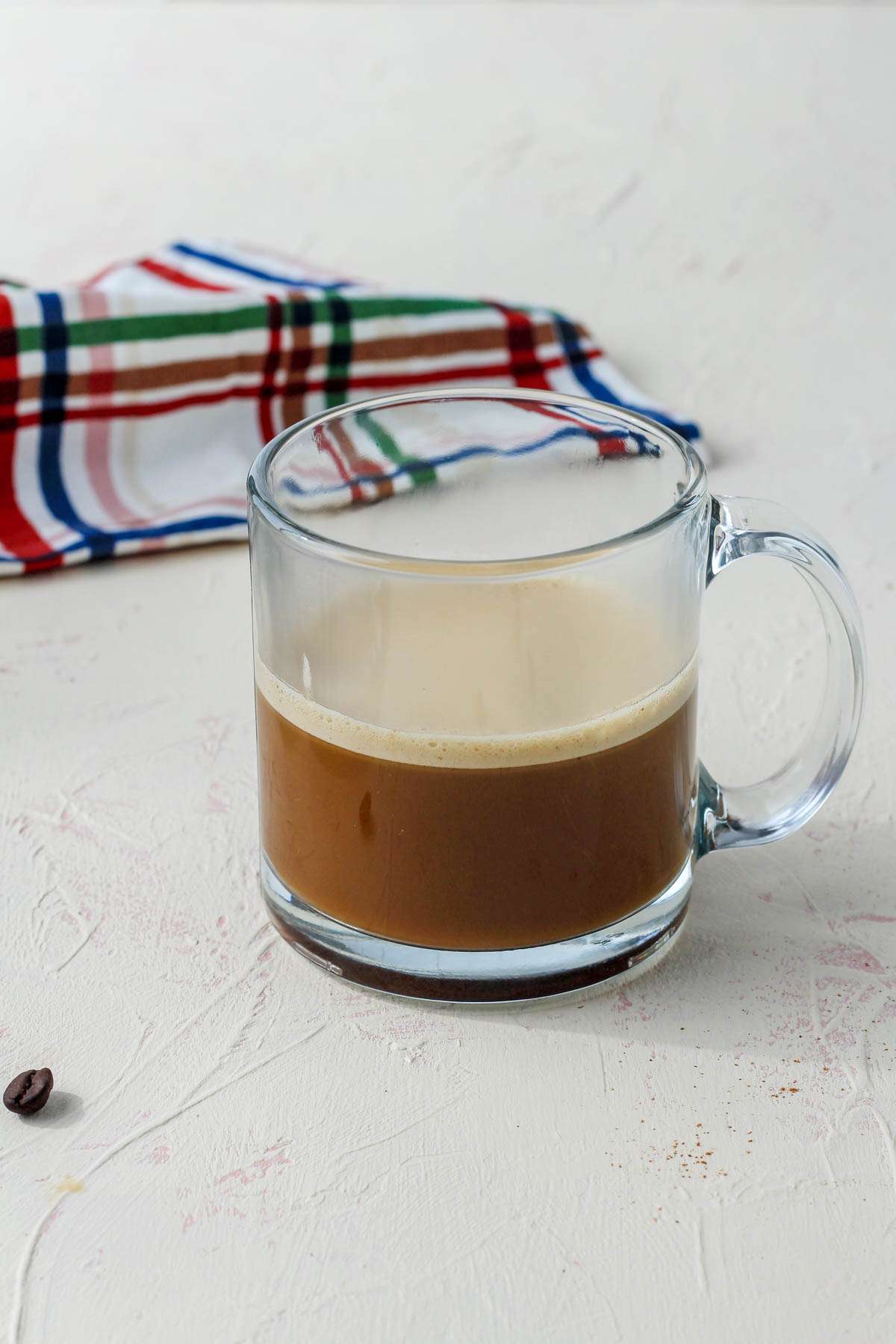 A glass coffee mug with vegan bulletproof coffee on a cream counter.