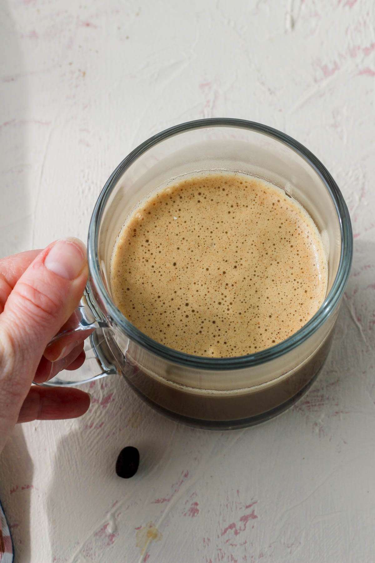 A hand holding a glass mug with vegan bulletproof coffee.