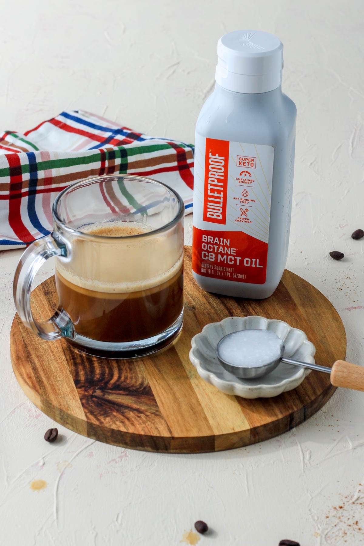 A wooden cutting board with a cup of bulletproof coffee on the left and a bottle of MCT oil on the right.