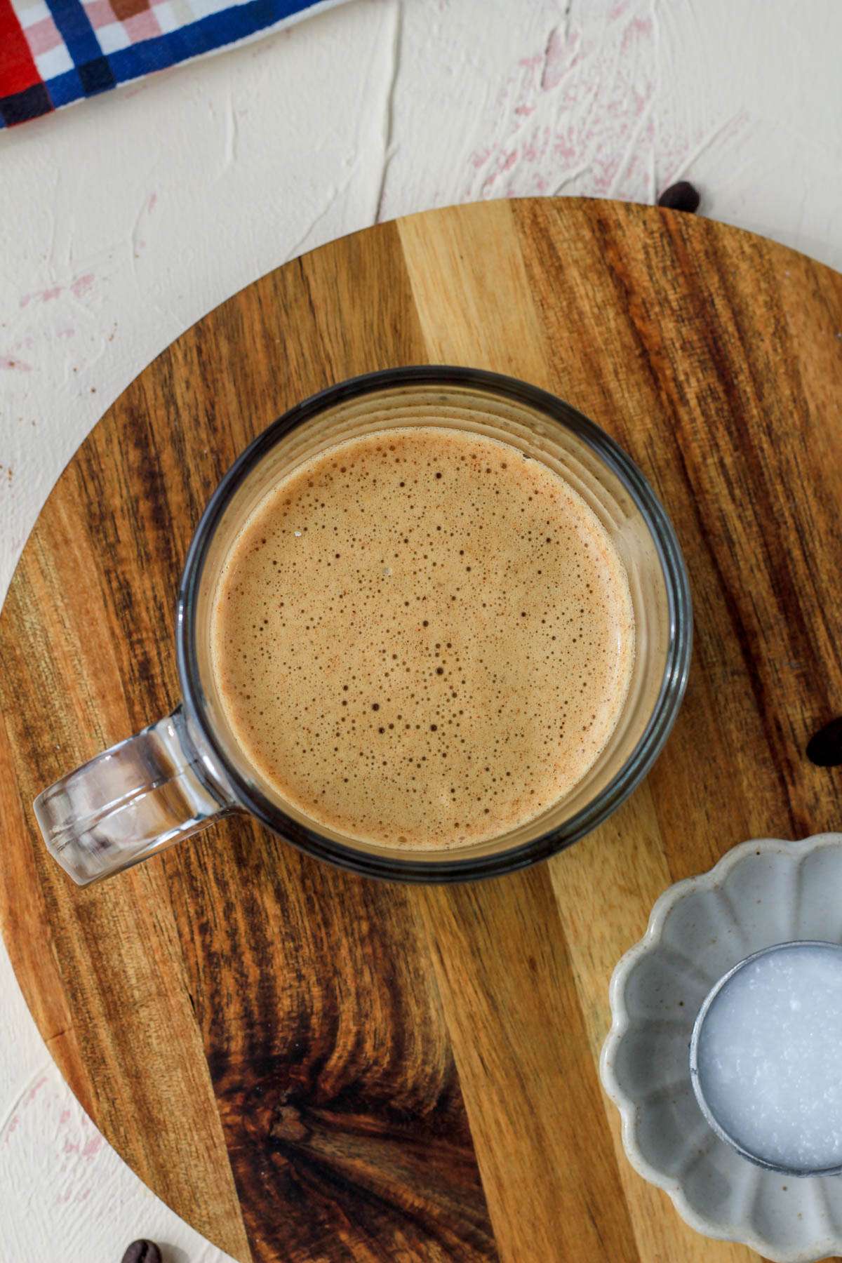 A top down picture of a wooden cutting board with a glass cup filled with bulletproof coffee.