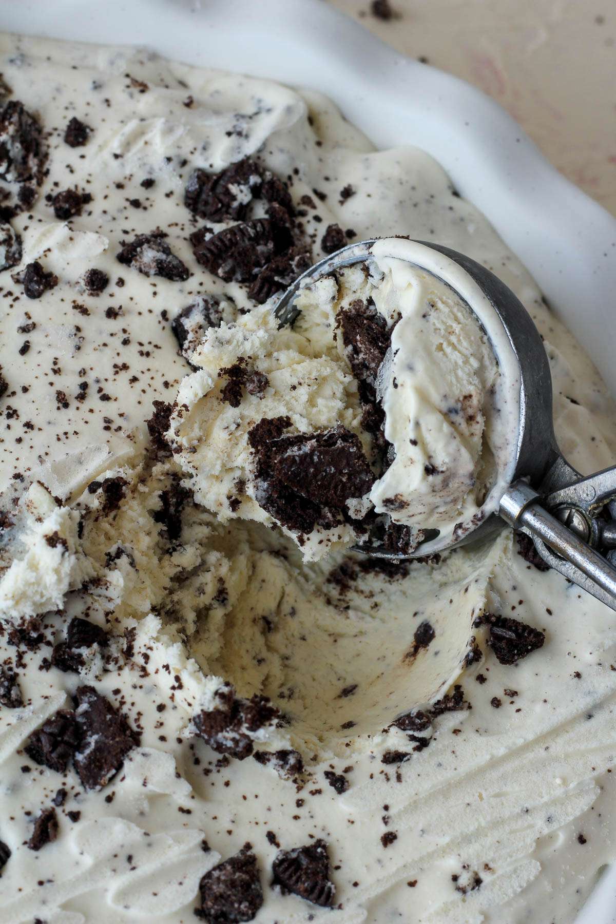 A silver ice cream scoop with a scoop of vegan no churn cookies and cream ice cream.
