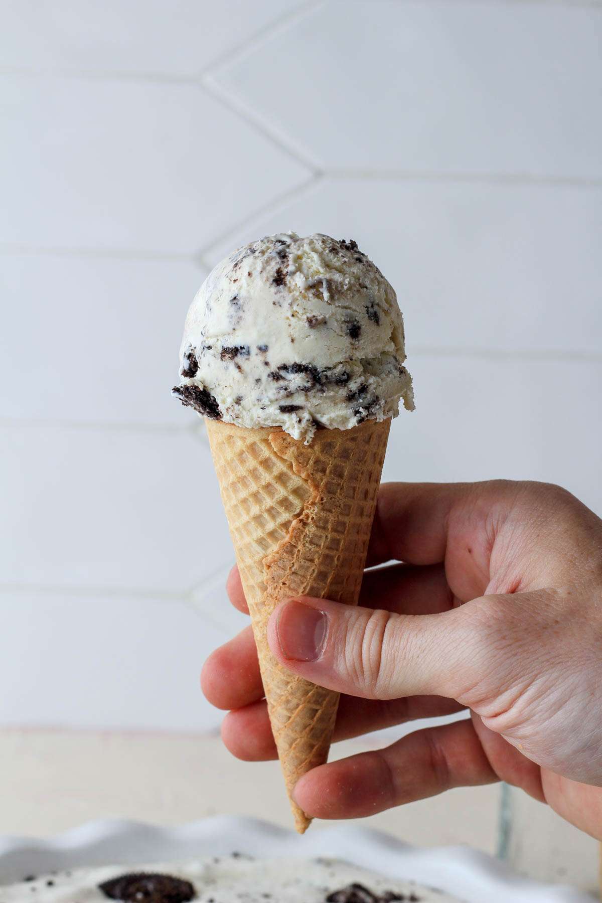 A hand holding a sugar cone filled with vegan no-churn cookies and cream ice cream.