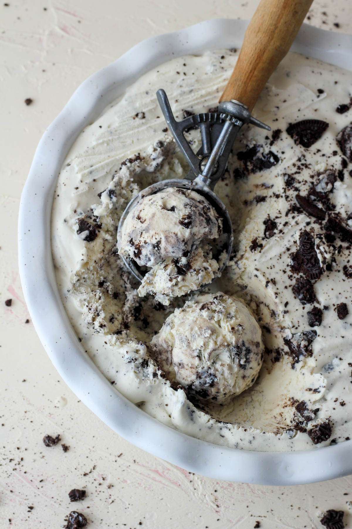 A top down picture of a white pie pan filled with vegan no-churn cookies and cream ice cream with a silver ice cream scoop holding a scoop in the top left of the pan.