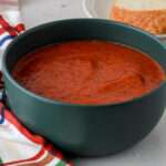 A close up of a thick bowl of dairy-free tomato soup in a dark green bowl.