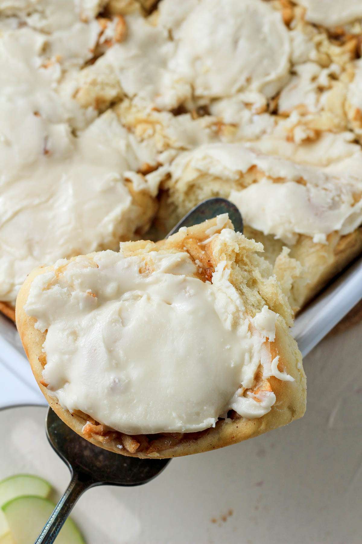 A spatula holding an apple pie cinnamon roll over the pan of cinnamon rolls.
