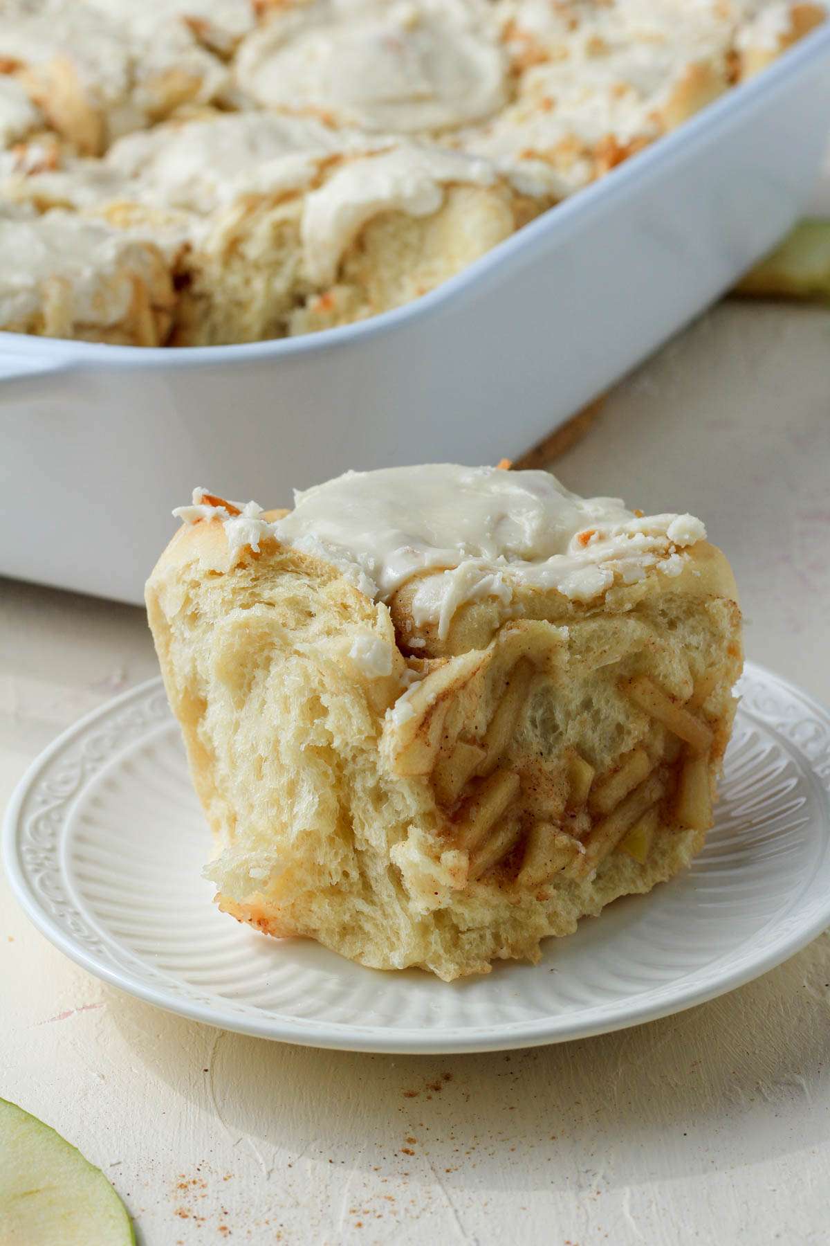 A white plate with an apple pie cinnamon roll from the side.