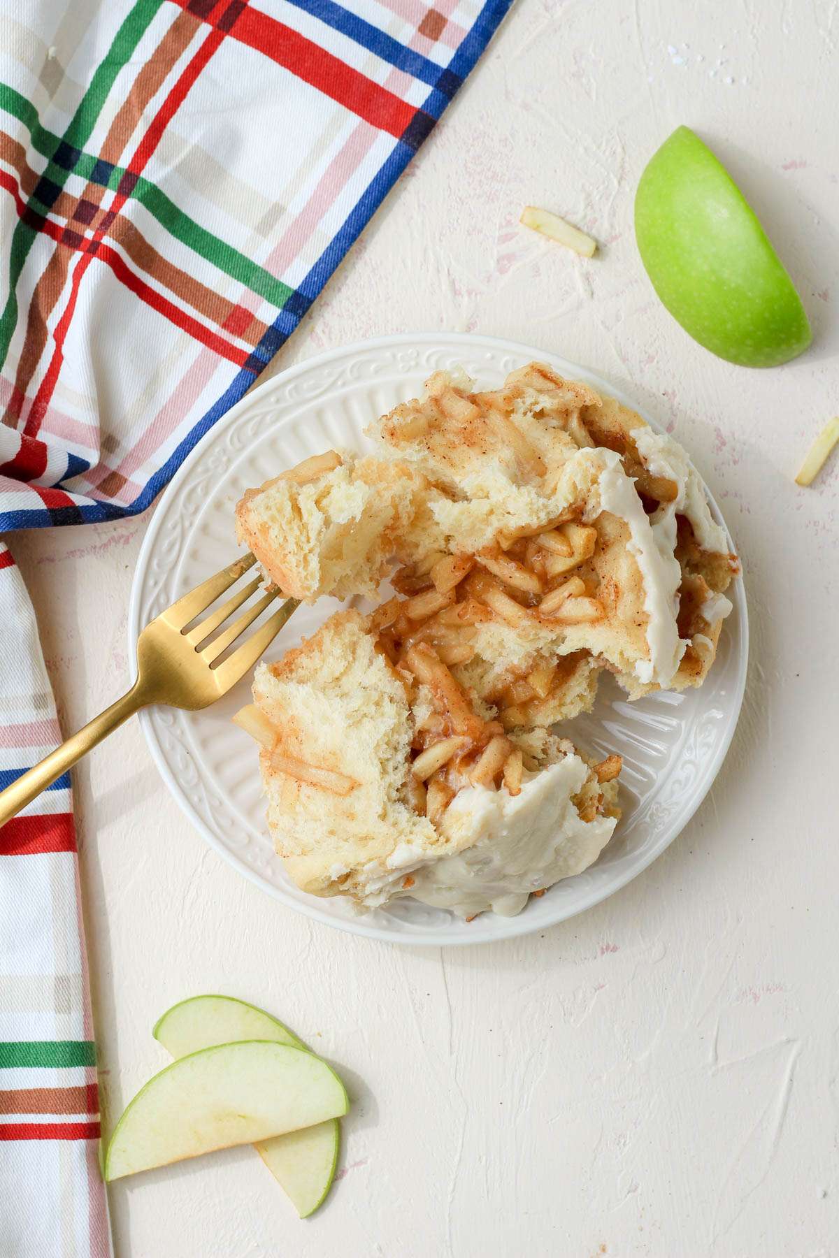 A white plate on a cream counter with a gold fork and an open apple pie cinnamon roll.