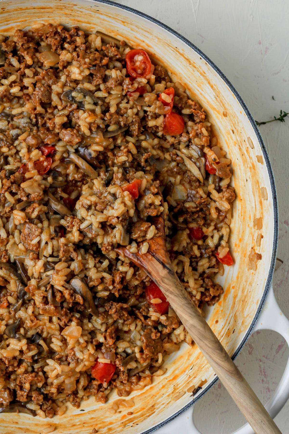 The right side of a white skillet with a wooden spoon or chorizo and mushroom risotto.