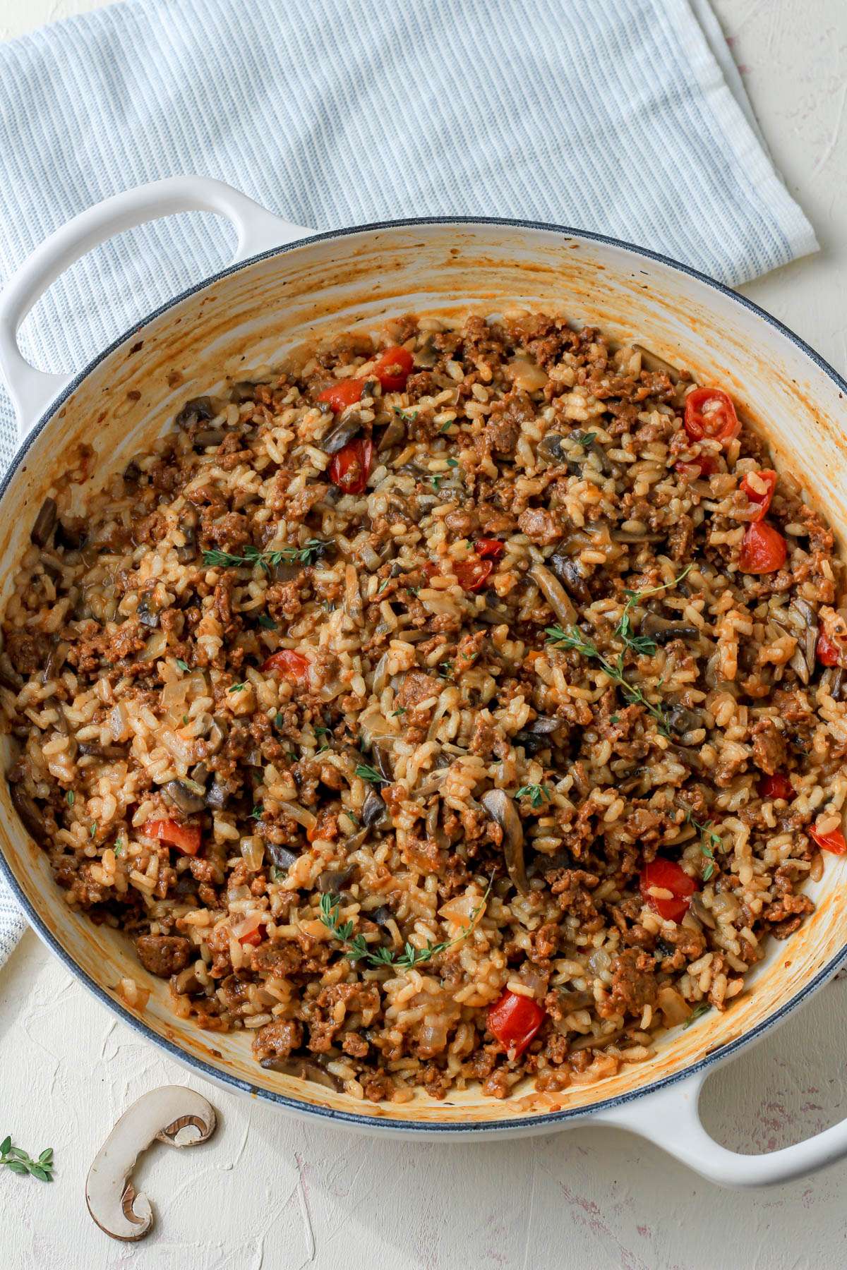 A top down photo of dairy-free chorizo and mushroom risotto in a large white skillet on a cream counter.