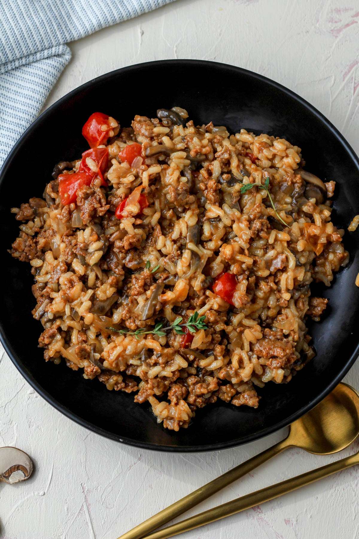 A black bowl with a serving of dairy-free chorizo and mushroom risotto with two gold spoons in the bottom right of the picture.