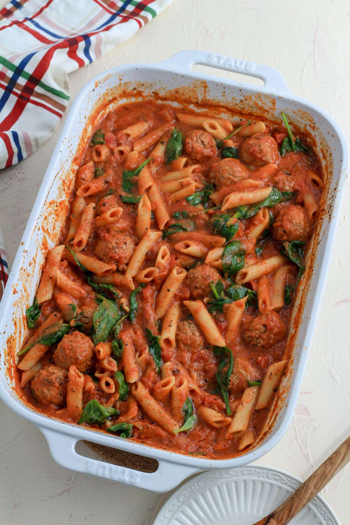 A white baking dish with dairy-free baked penne with meatballs on a cream counter.